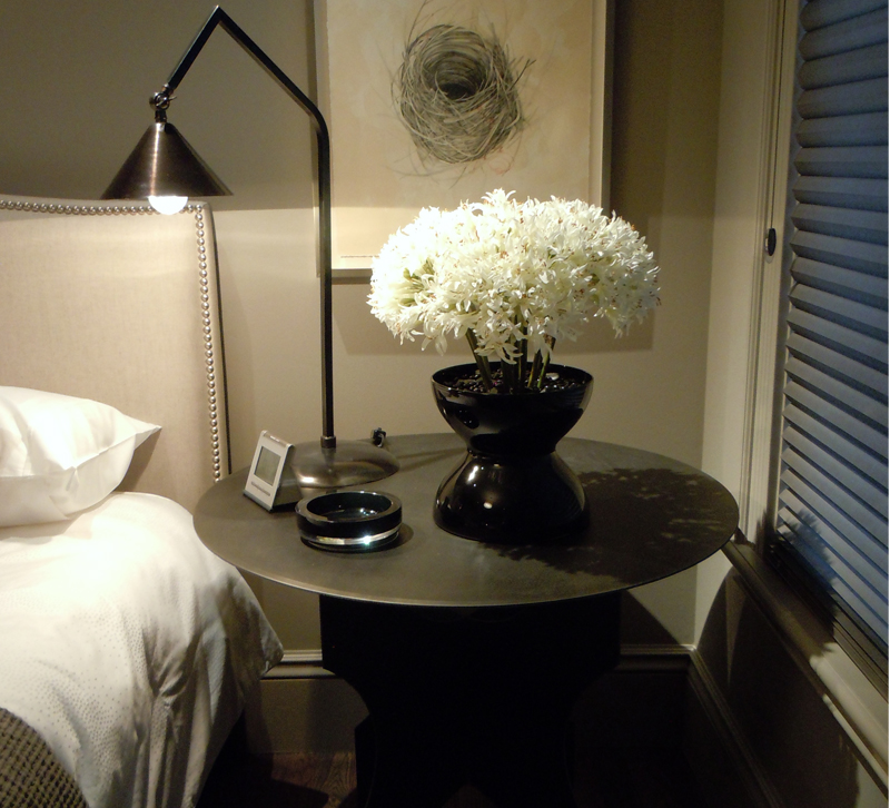Table with flowers and table lamp next to bed