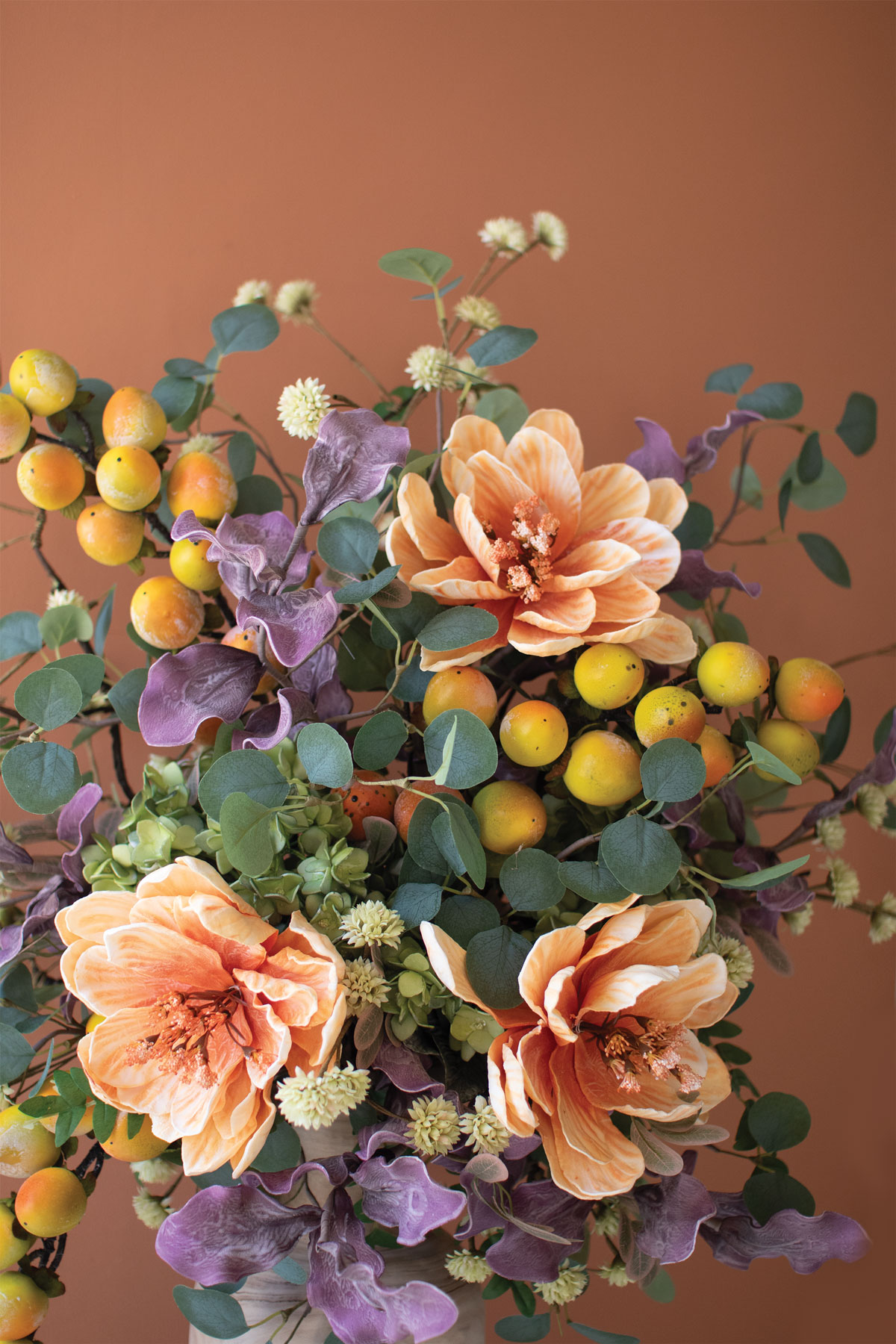 large purple and pale orange flowers, greenery, small white flowers, and small yellow and orange fruit in a vase