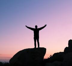 Man standing out rock with arms stretched out at sunset