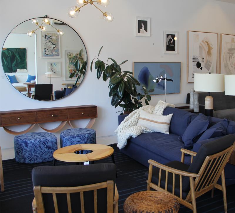 Living room setup in Consort Design showroom with a blue sofa and round wall mirror