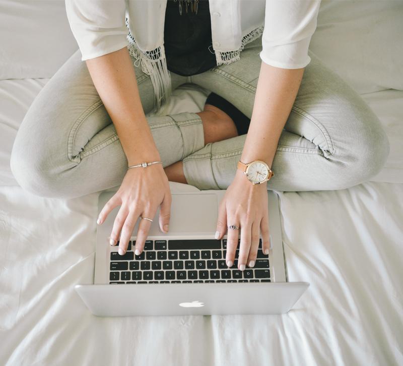 Blog writer sitting crosslegged on bed and writing on laptop